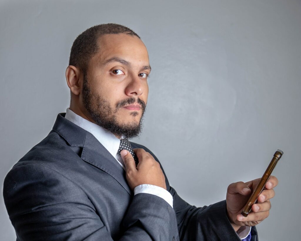 Successful male entrepreneur in formal wear confidently looking at camera while lounging in bright room with smartphone